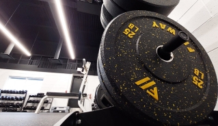 Closeup of a 25 lbs weight plate on a rack with smaller weights on racks in the background.