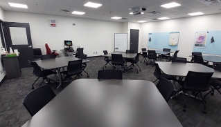 Centre for Adult Learning Brandon classroom with light-blue boards on the walls and dark grey square tables.