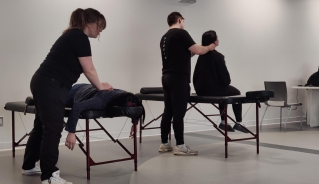 Two people getting massages from two masseuses on foldable massage tables in a room with white walls.