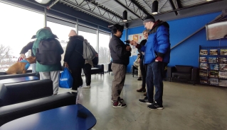 A group of people in winter jackets standing in a room with a blue wall and large windows, petting dogs and smiling.