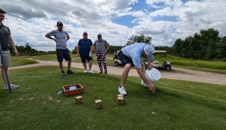 A player rolling big wooden dice on the green while his team is watching.
