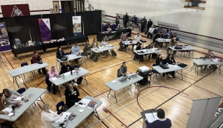 Photo from above of the counsellors sitting at tables at the gym, listening to a presentation.