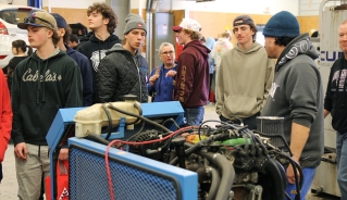 A group of male high school students standing in front of an exposed car engine.