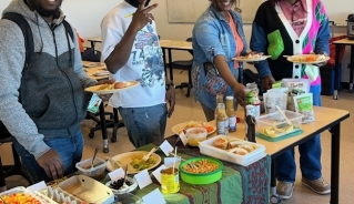 Four students standing in front of a table full of food with plates and smiling.