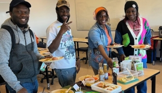 Four students standing in front of a table full of food with plates and smiling.