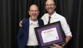 Graham Street posing with his award certificate in front of a black curtain with another person standing next to him.