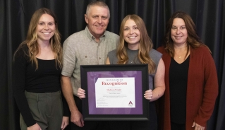 Madison Wright posing with her award certificate in front of a black curtain with a group of people.