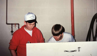 Warren Cowling and another person looking down at something in a farm machinery shop.