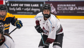 Assiniboine hockey player focusing on the puck during a game.