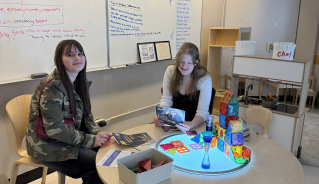 Two prospective students sitting at a lit up table with magnetic toys and information sheets in an ECE classroom.