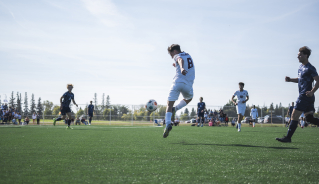 Assiniboine men's soccer player kicking the ball in the air during a game.
