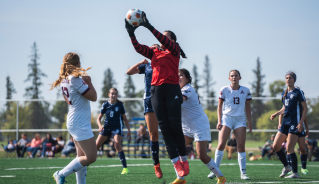 Women's soccer team goalie in a red shirt catching the ball.