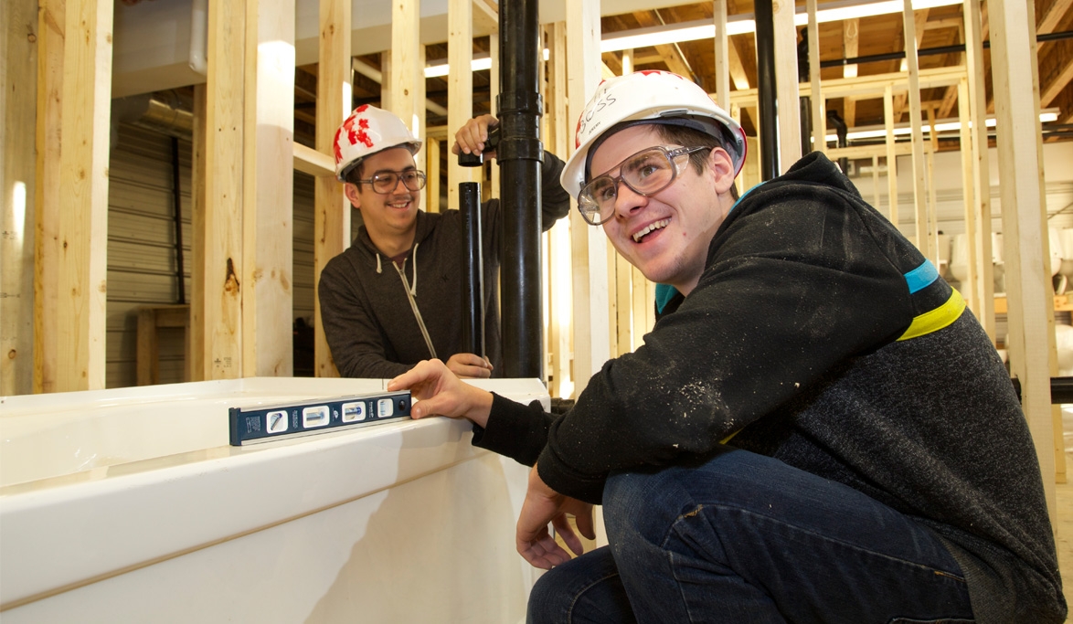 two piping students kneel inside trades shop