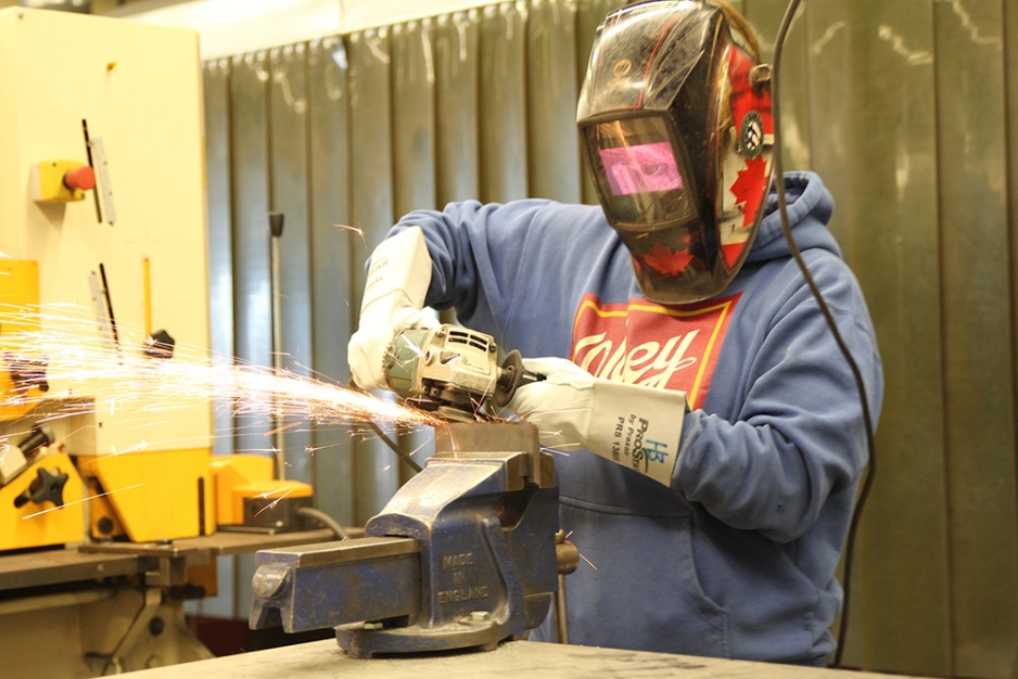 Heather Bruederlin grinding metal in trades shop.