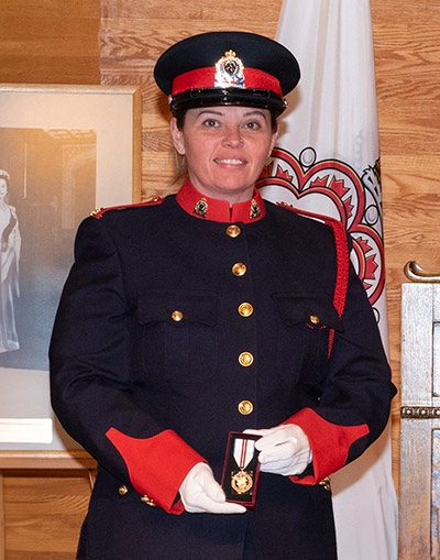 Amanda wearing a uniform, holding a medal with a white ribbon and two red stripes on it