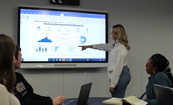 A student presenting Marketing stats on an interactive board in the new Westoba Lab to three other students.