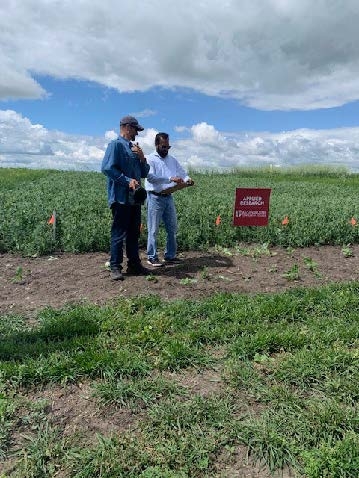 Dr. Baljeet Singh standing with another person in a field of greenery near an "Applied Research" sign.