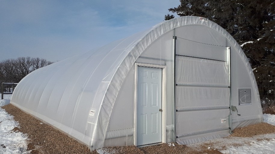 Photo of the outside of the high tunnel structure with snow lying around it and trees in the background.