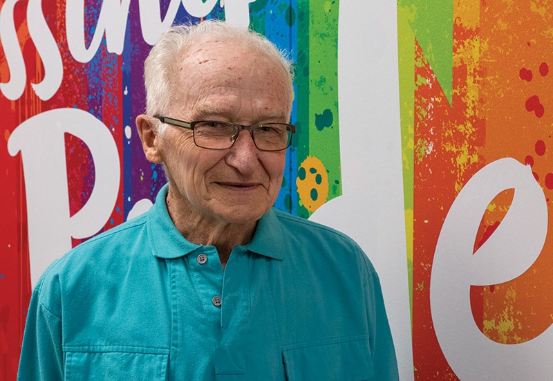 Frank Watt standing in the hallway in a blue shirt and smiling at the camera.