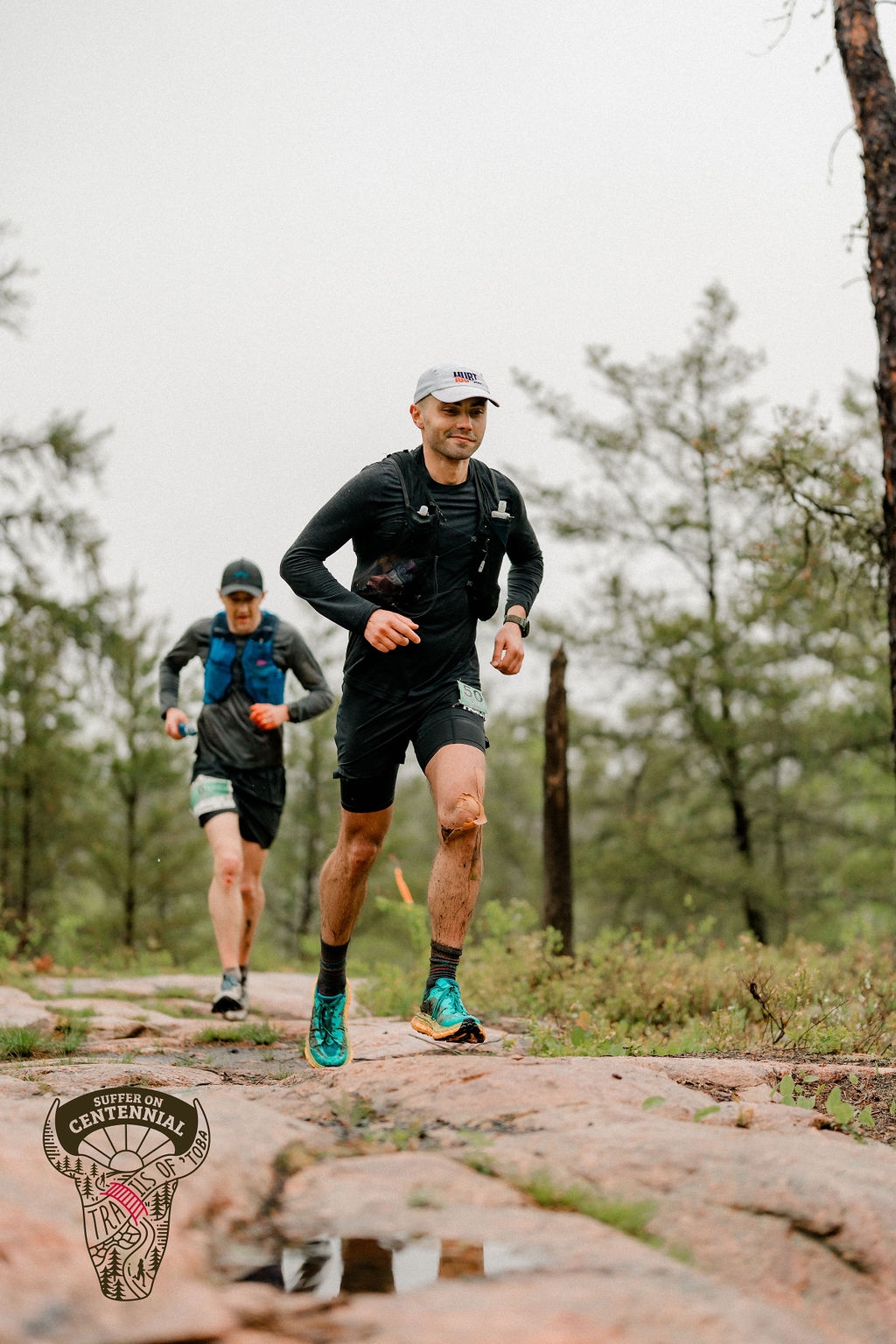 Ihor Verys running and smiling on a trail with another runner behind him and trees all around.