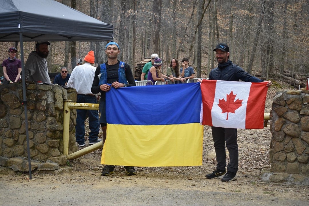 Ihor Verys standing with a Ukrainian flag near a group of people behind metal barriers.
