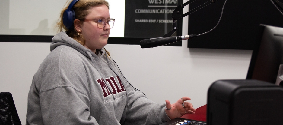 A CJ106 radio station volunteer sitting in front of the microphone and mixer during a live show.