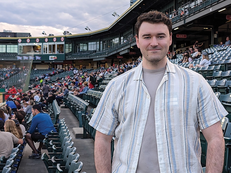 Daniel Moss standing in the bleachers of a stadium full of people.