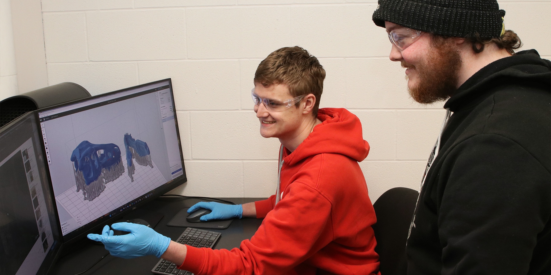 A person sitting in front of a computer, showing another person a digital version of a 3D model.