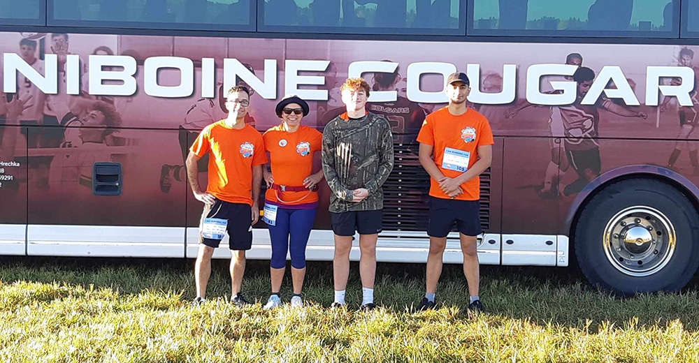 A group of four people standing in front of Assiniboine Cougars bus in athletic attire.
