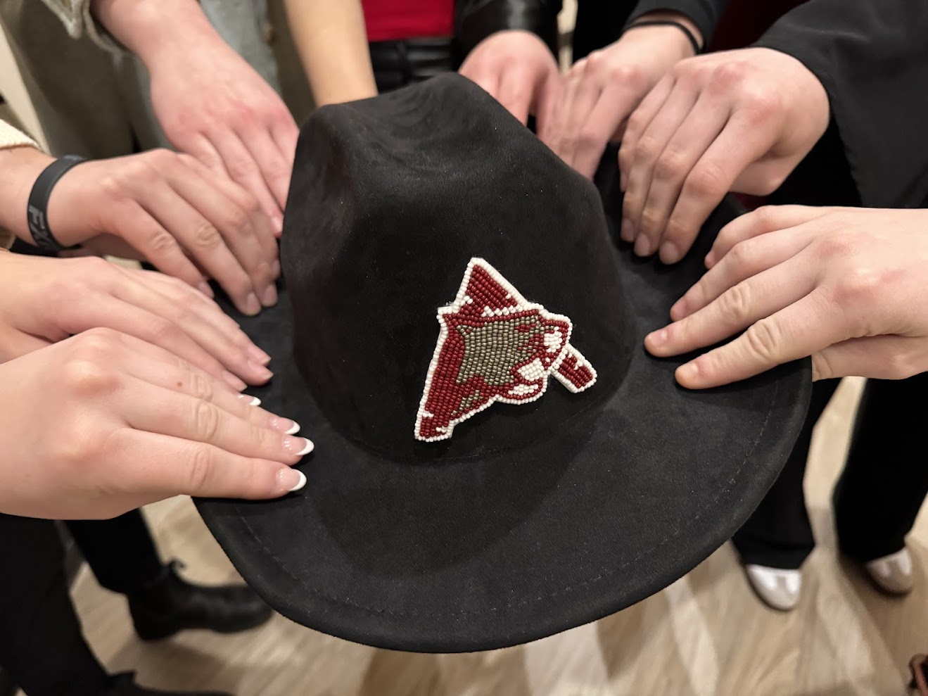 Indigenous student athletes holding a black beaded hat with Assiniboine Cougars logo