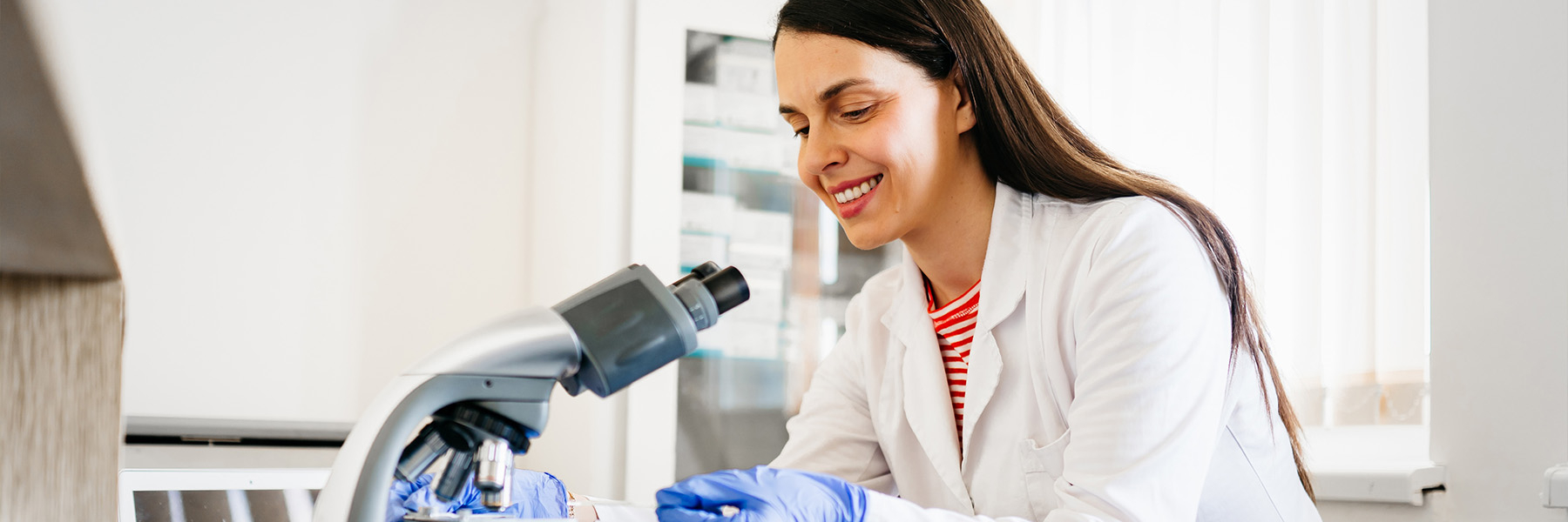 A woman in a lab coat putting a slide into a microscope.