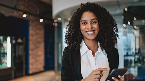 A woman dressed in a white shirt and black cardigan standing with a phone in a brick office space.
