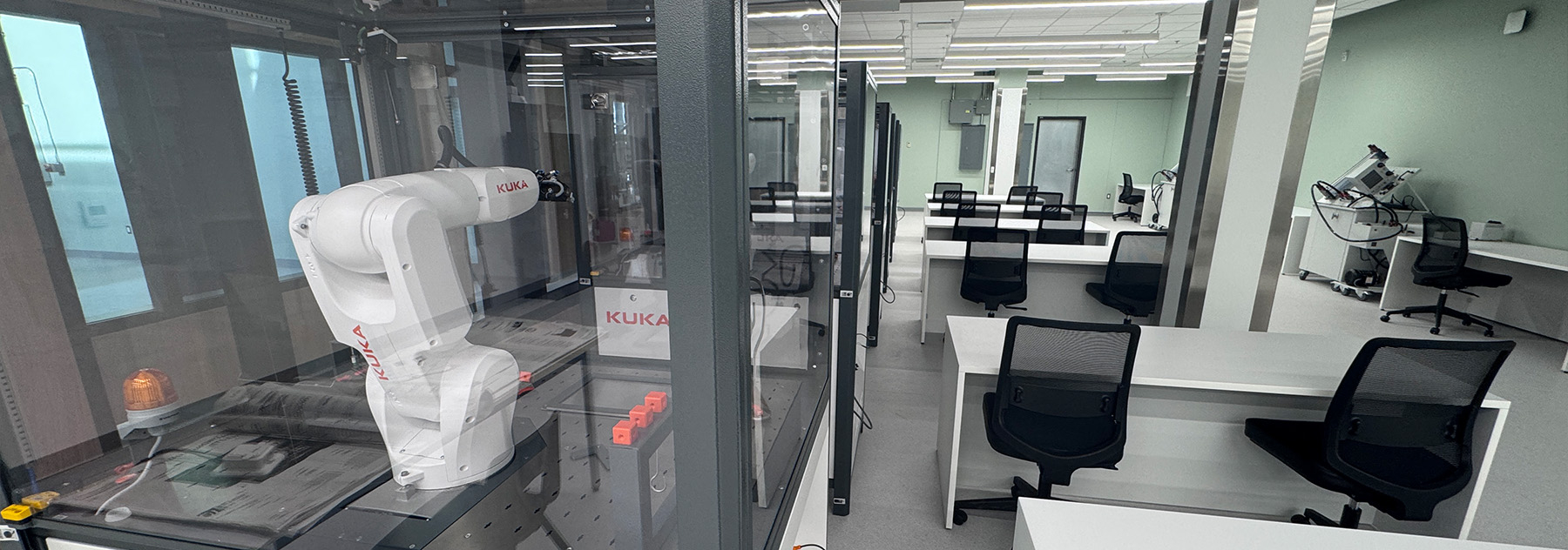 A room with a row of robotic arms on the left side and desks on the other side.