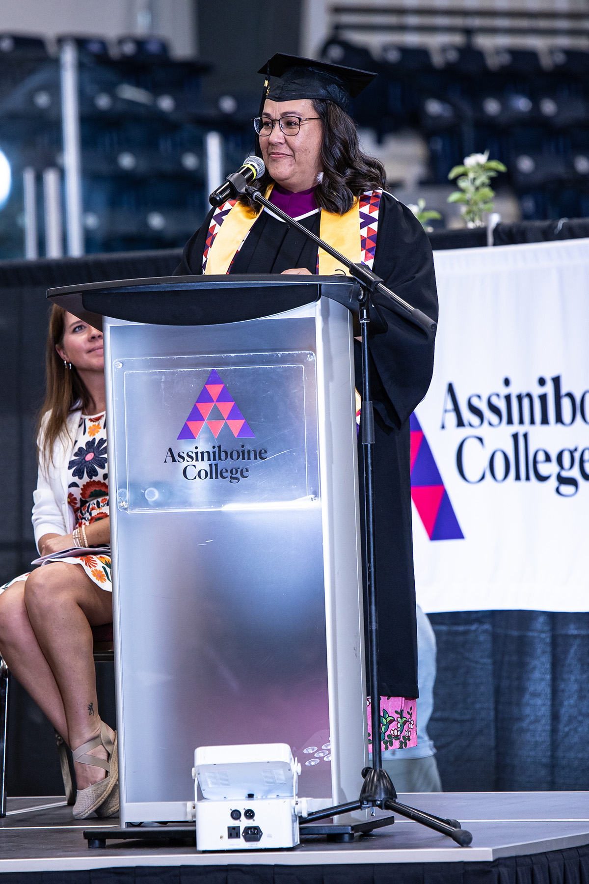 Tammy Chief standing at the podium during graduation in a gown and Valedictorian sash.