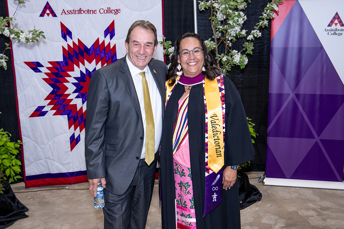 Tammy Chief posing with a man in front of the Assiniboine quilt and banner at graduation.