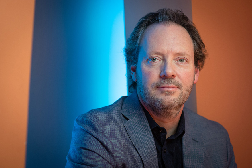 Brad Mahon portrait photo with a blue, grey and orange background.