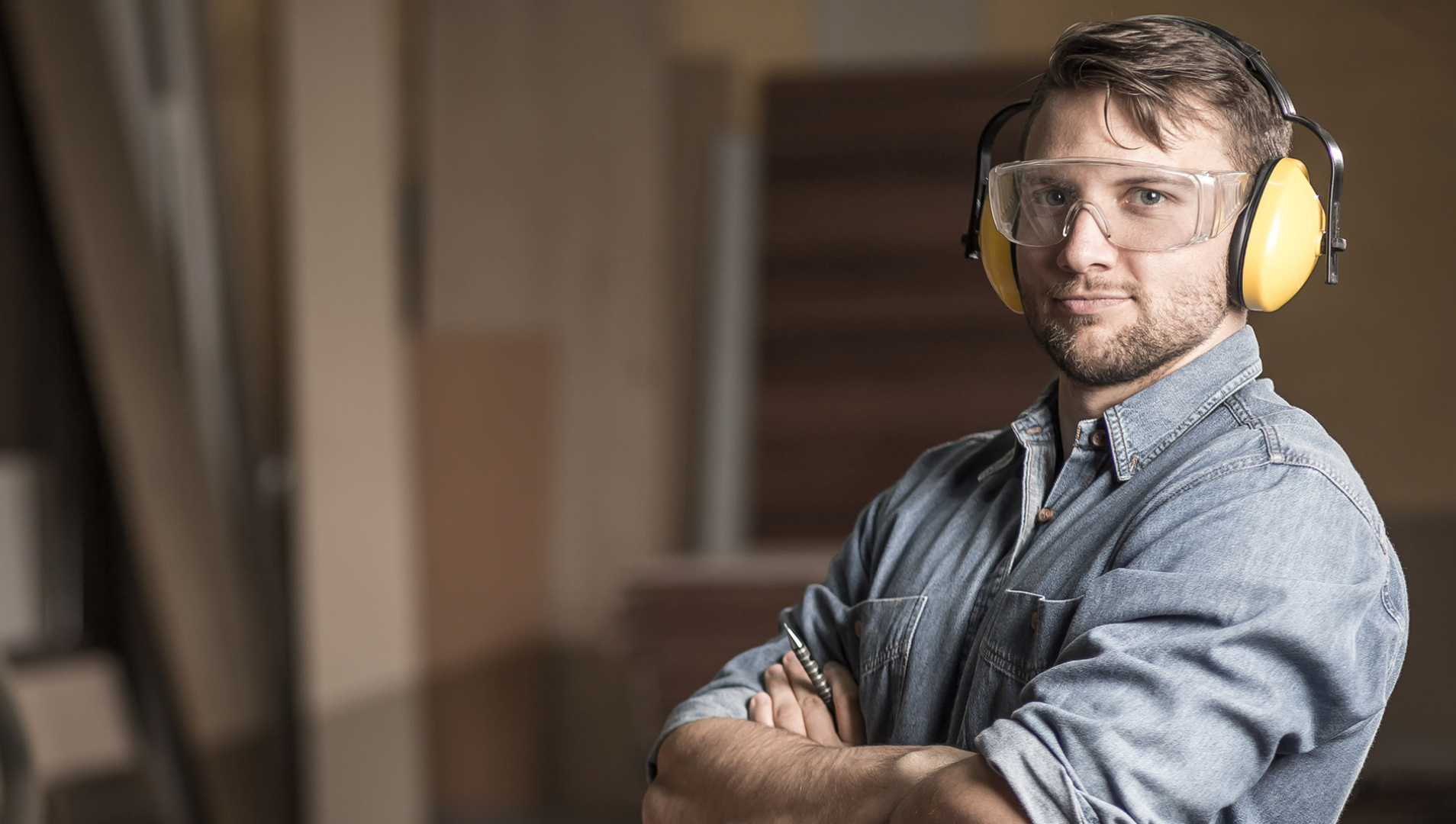 A man with arms crossed while wearing woodworking protective equipment.