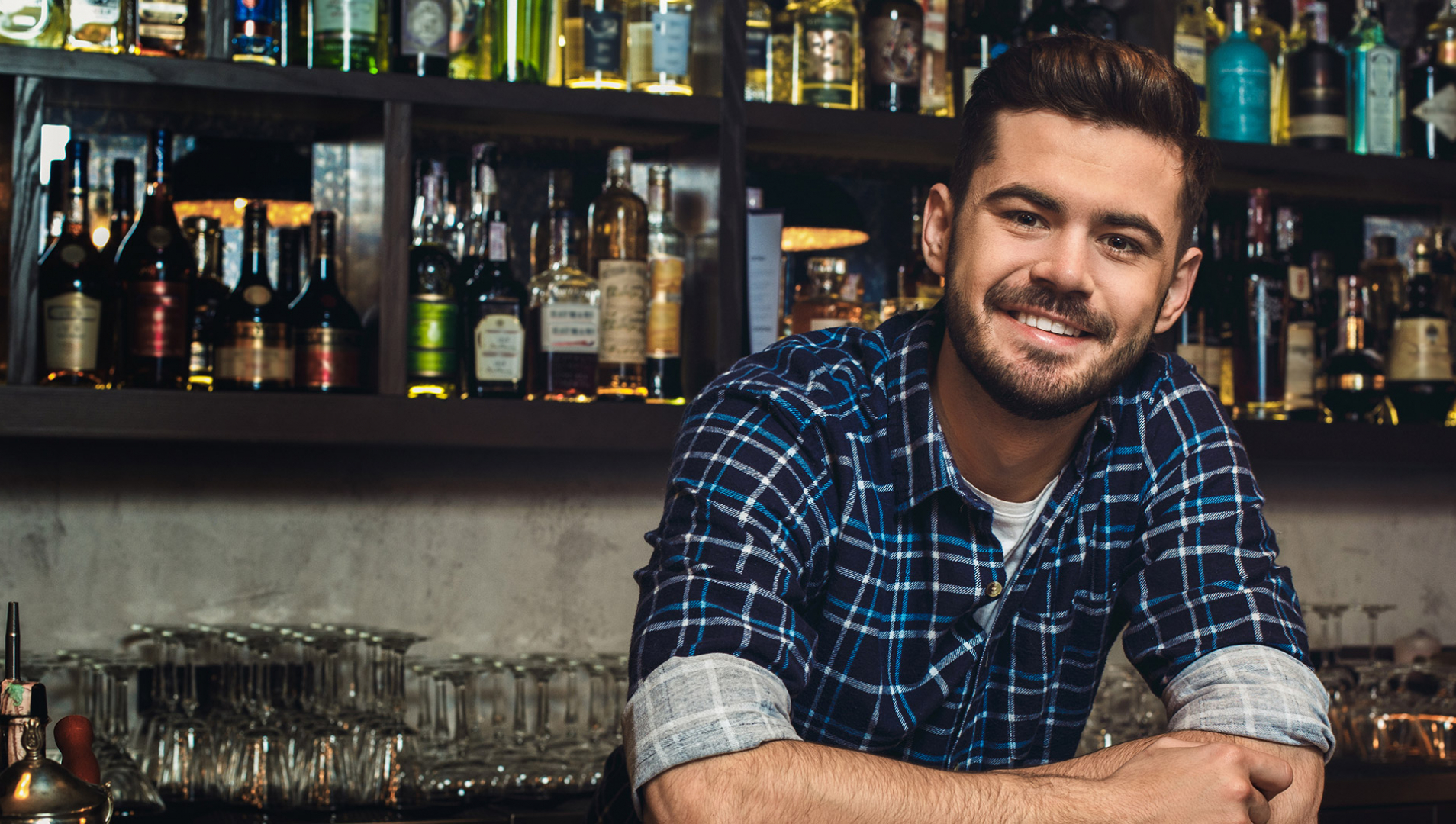 A male bartender smiling while working at a bar.
