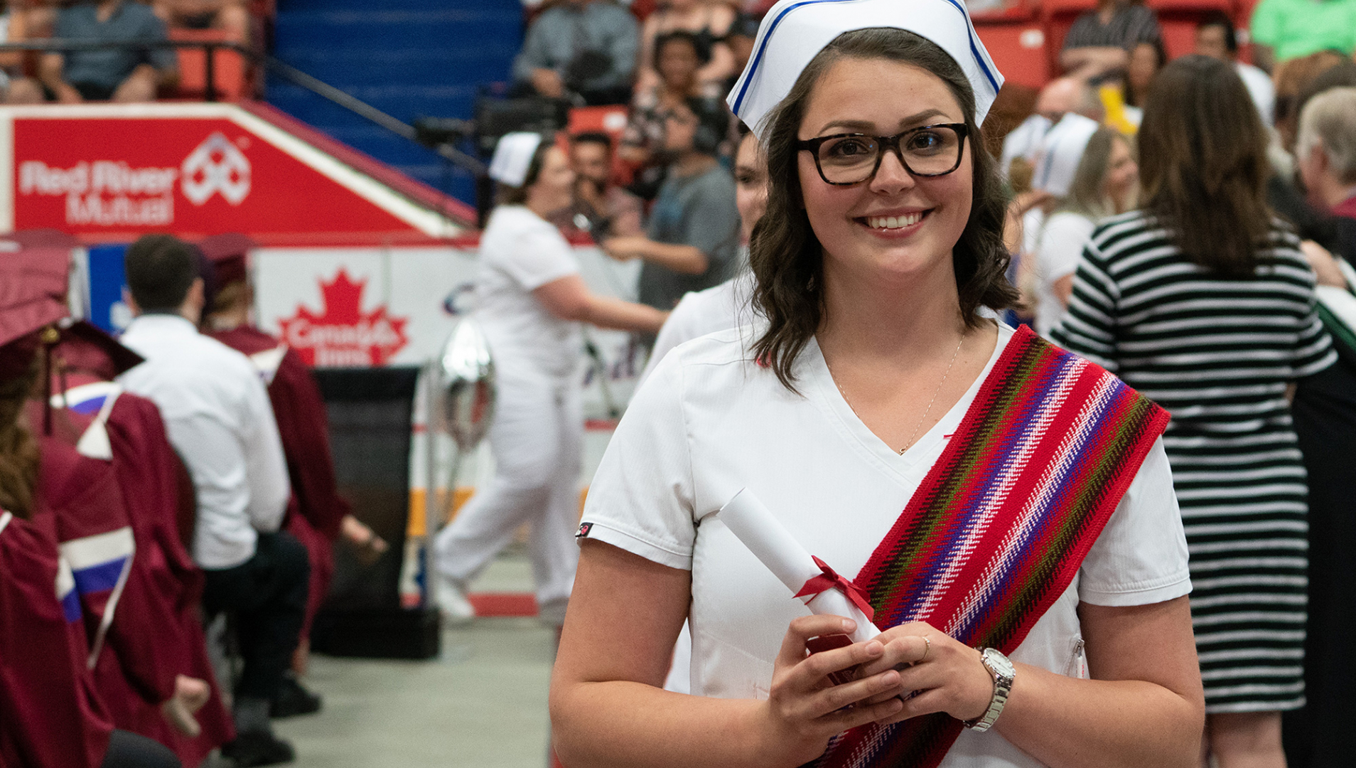 Nursing graduate stands smiling at camera holding diploma scroll.
