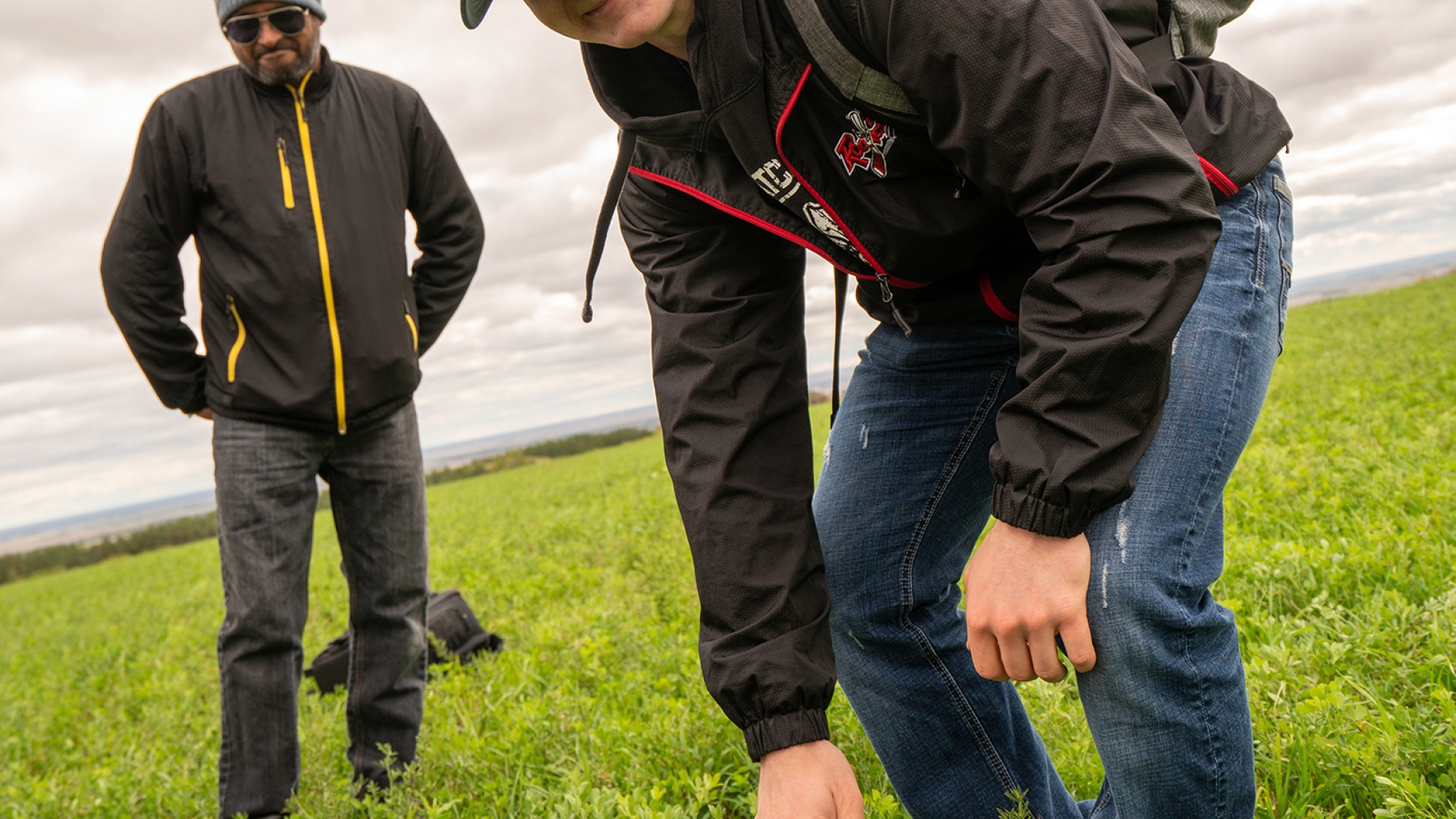 An agriculture student smiles while he does experiential work in the field as his instructor watches.