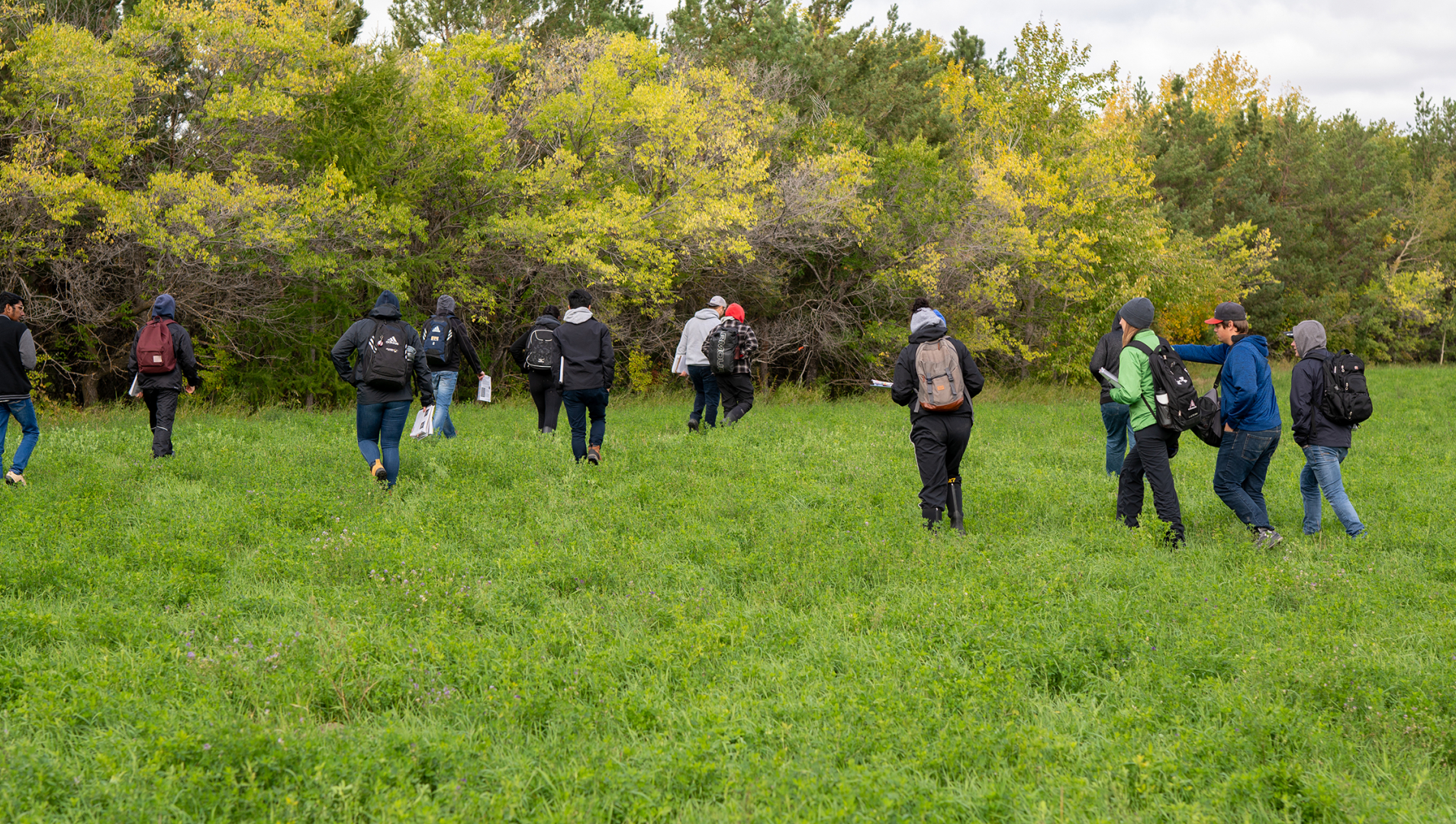 A group of ag students walk through a field with backpacks and notepads. 
