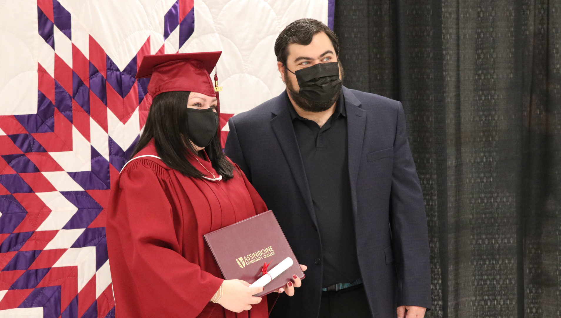 An Assiniboine graduate donning a cap and gown poses for a photo with a family member. 