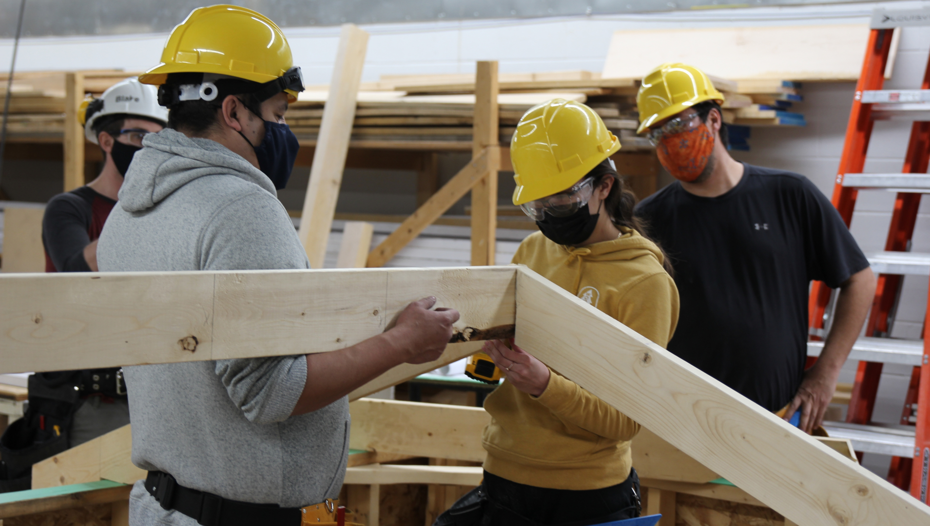 A group of four students, all in hard hats, work to assemble a piece of a building assignment