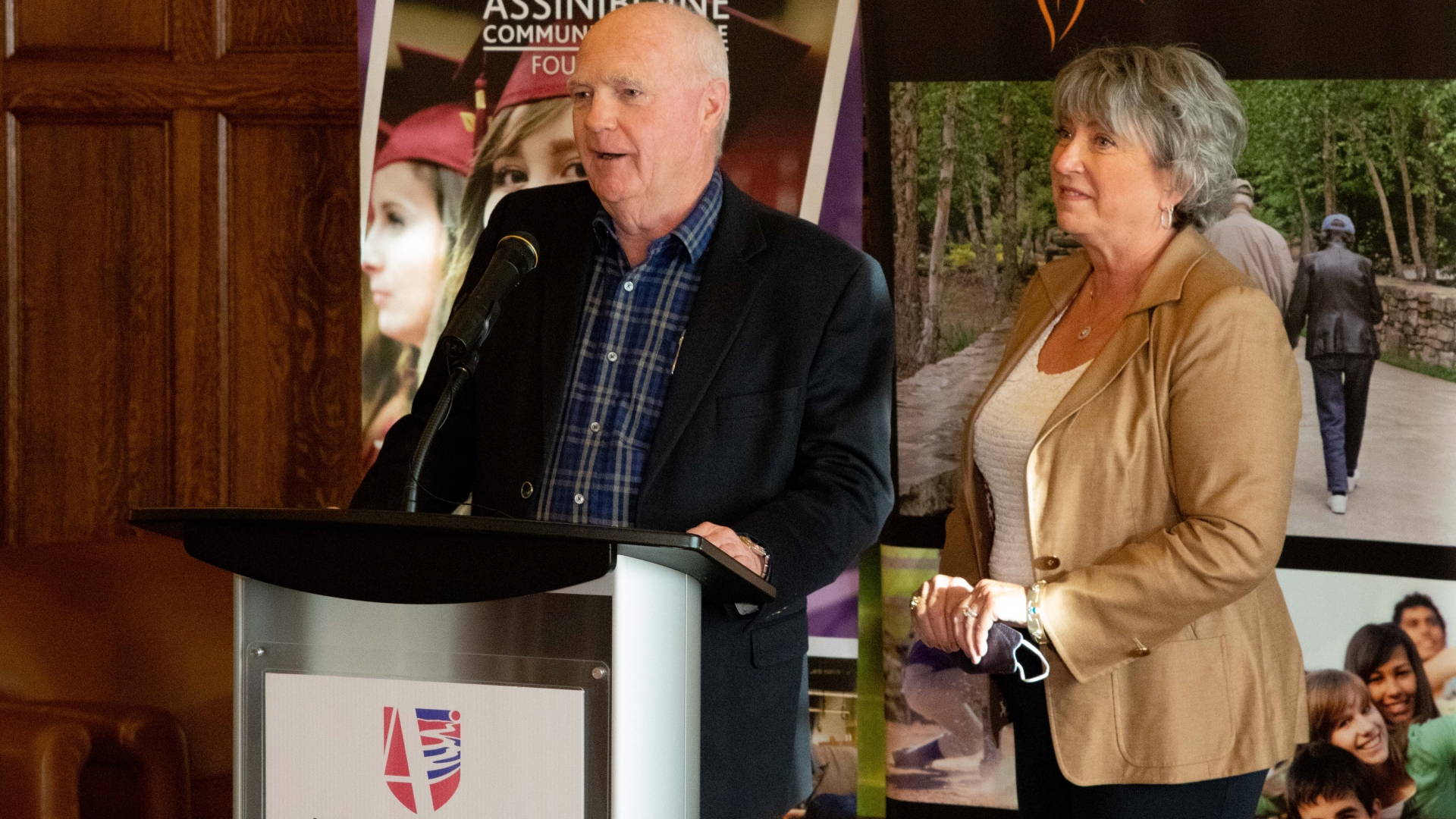Gord Peters stands at the podium in the left of the photo frame, with Diane Peters behind him in the right of the frame