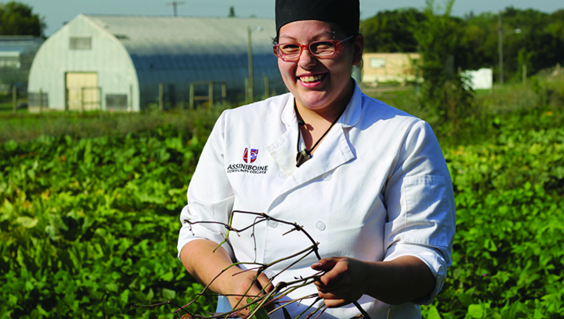 A student in a culinary uniform stands in the foreground of the photo before a field behind her. 