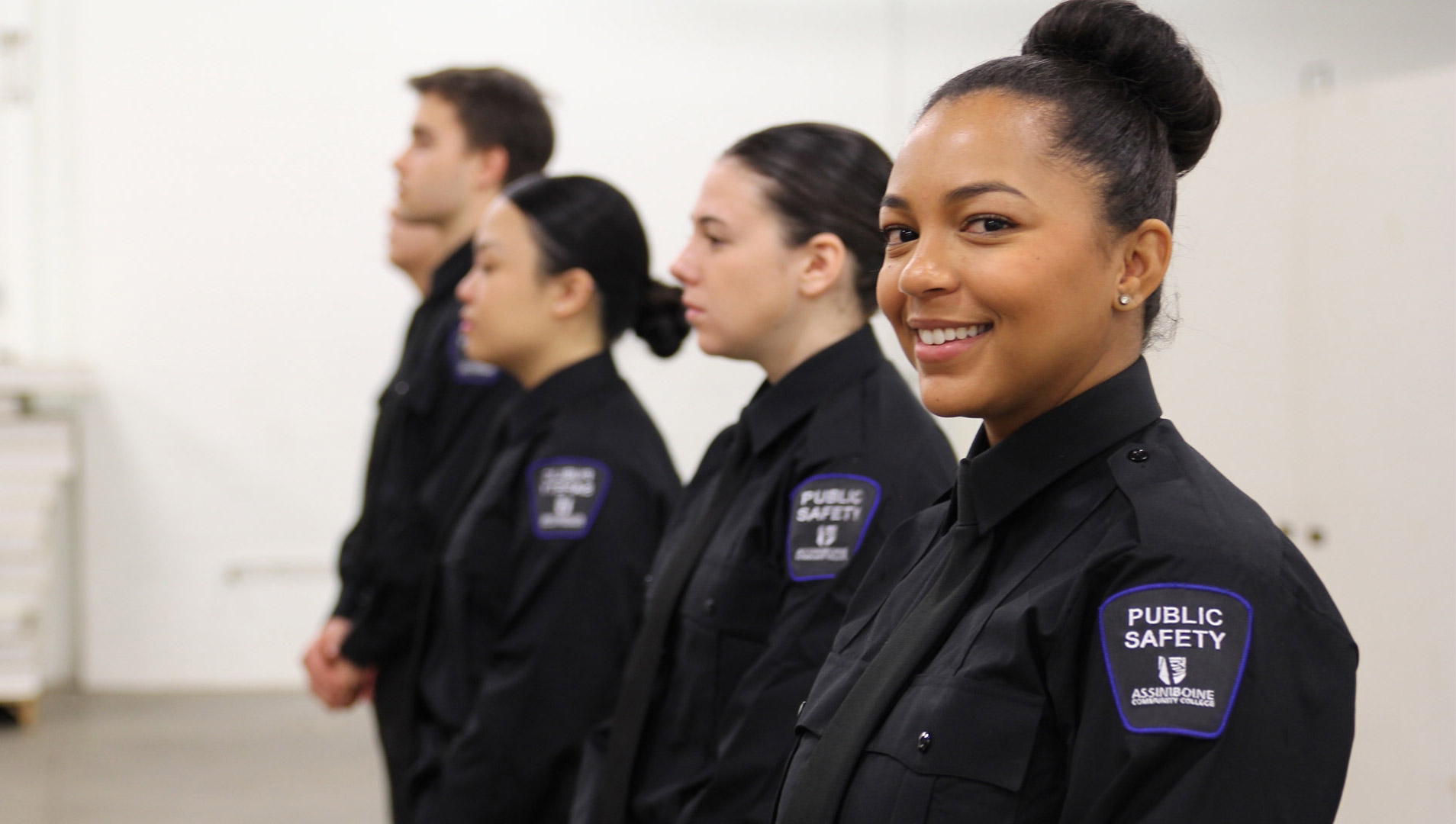 A lineup of Public Safety students in black uniforms, with the closest one smiling at the camera.