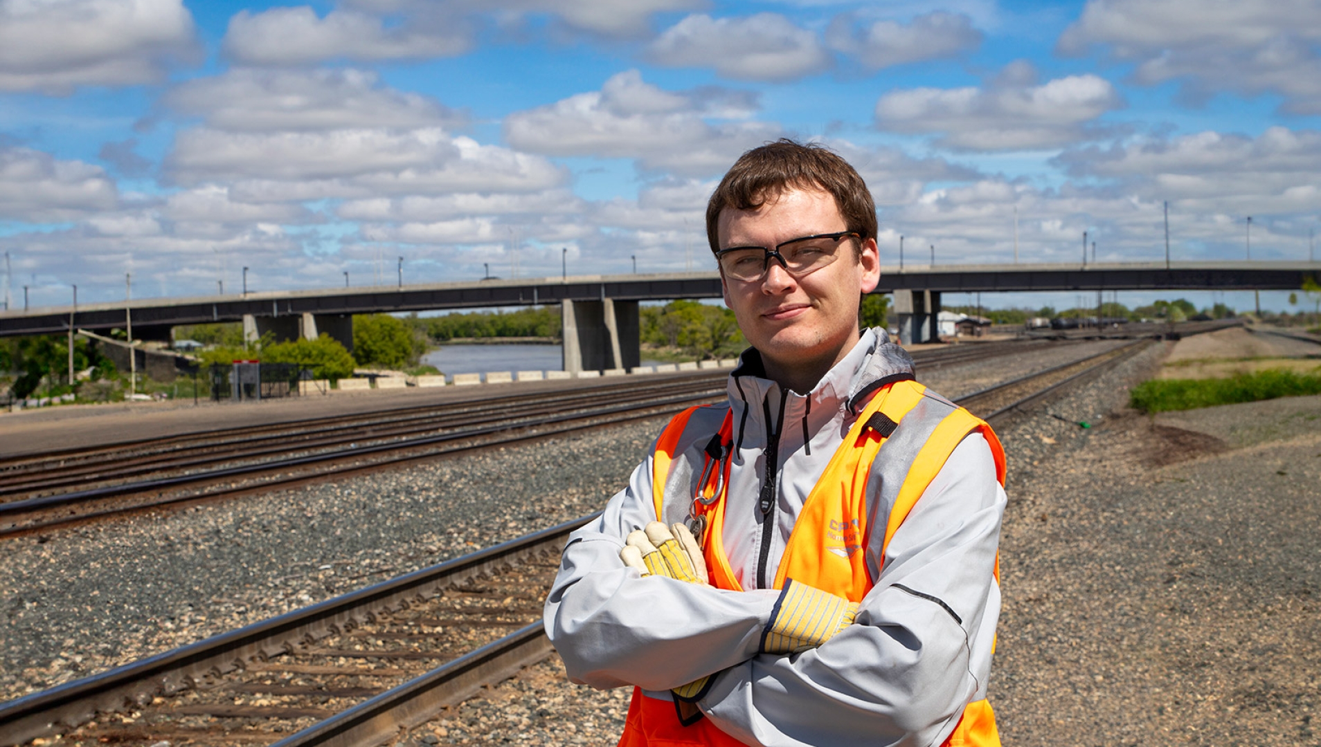 Jonn Olson standing in a high visibility vest with railroad tracks spanning in the background.