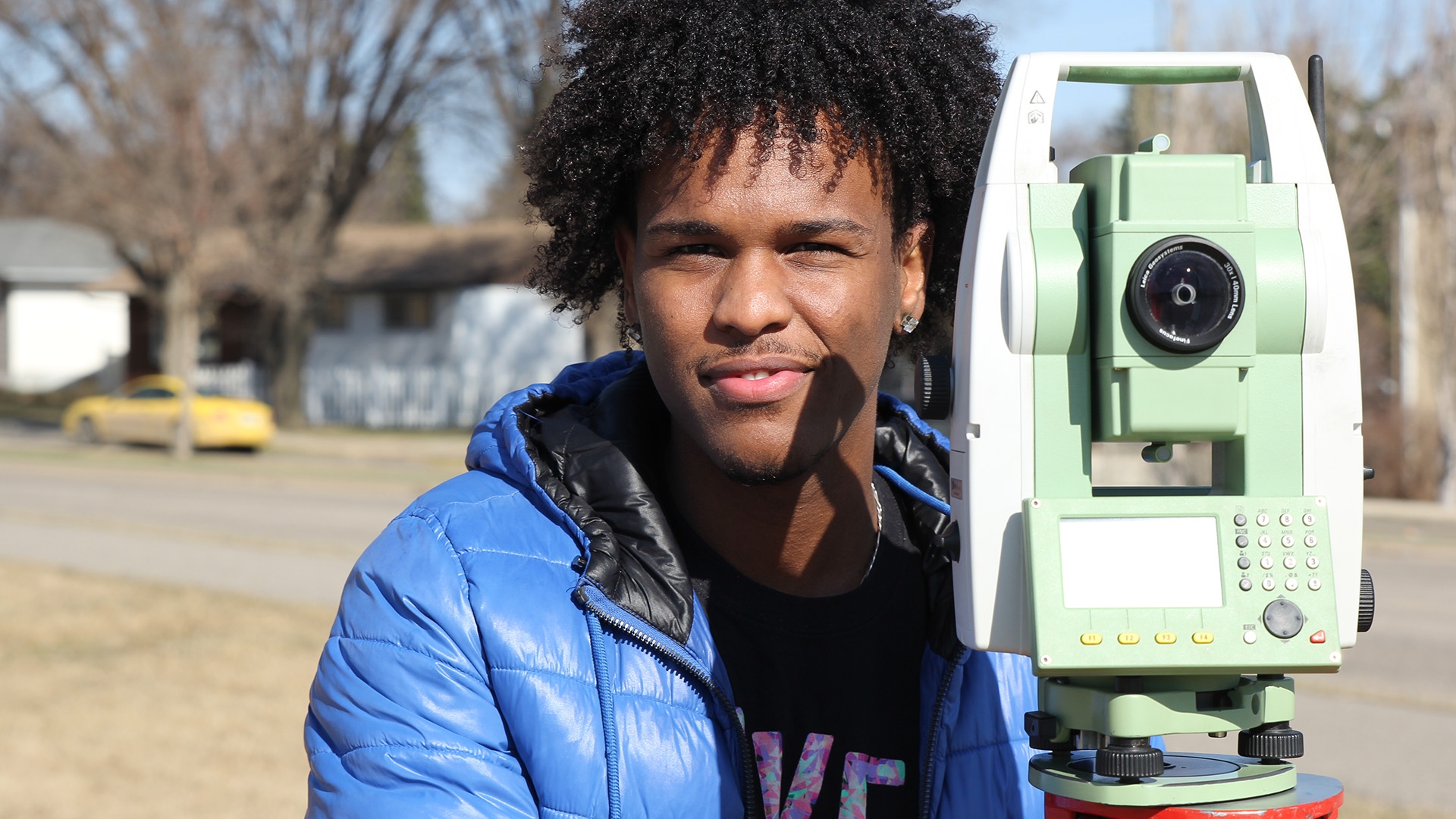 A civil technology student standing next to surveying equipment.