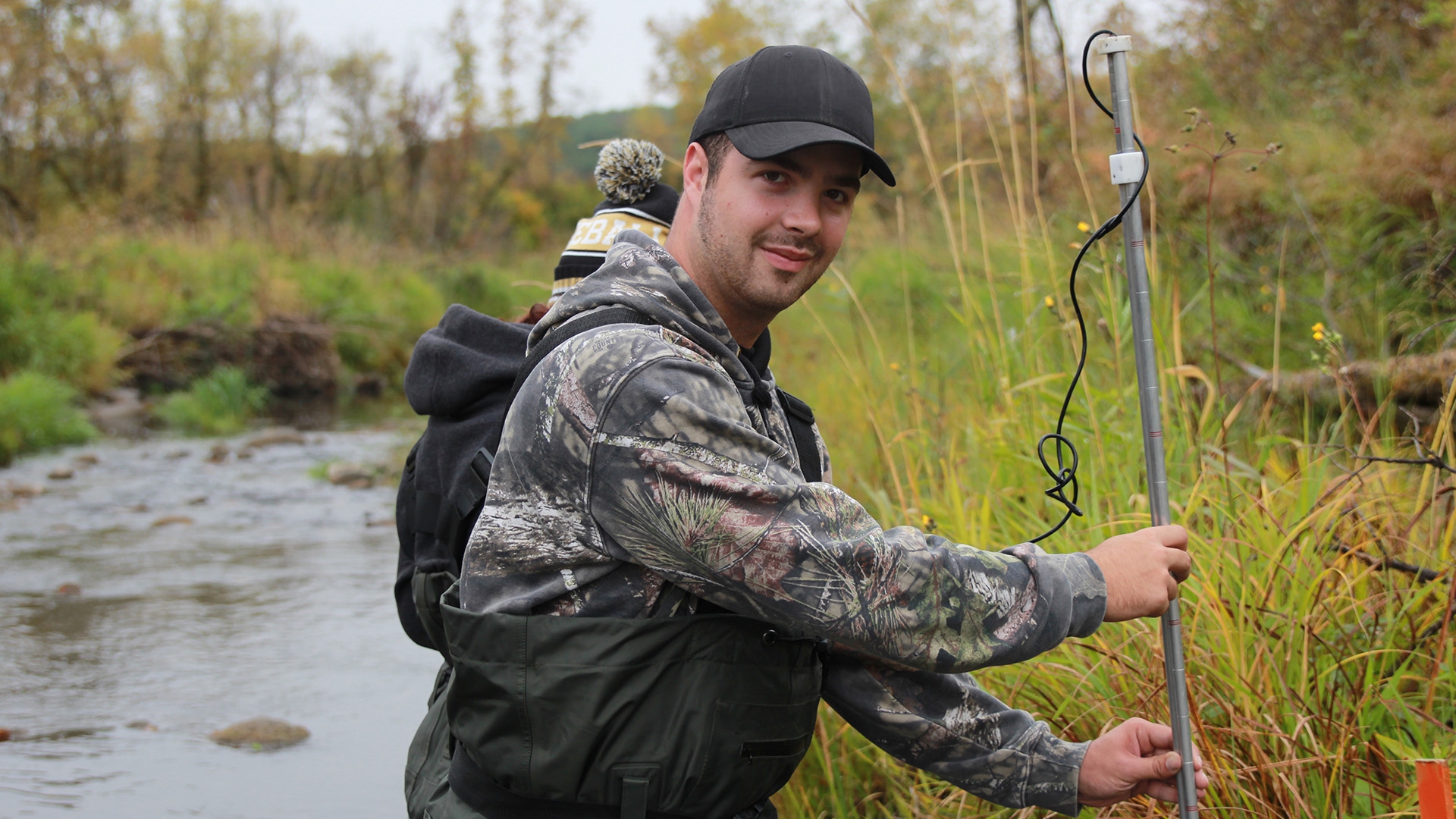 A student in camouflage clothing holding a metal measuring rod.