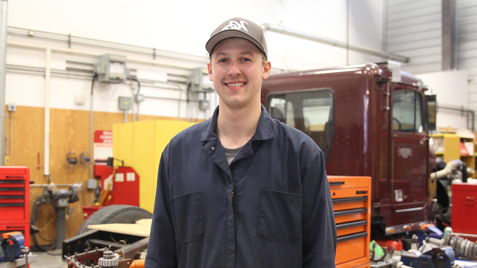 A heavy equipment technician student standing in front of a truck in a garage.